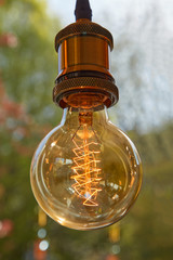 Eine Lampe h&auml;ngt im hellen Sonnenschein mit einem Garten als Hintergrund.