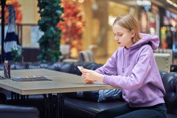 women sitting at a table waiting for friends, the girl looks at the phone.