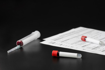 Two vacuum tubes for blood analysis with a blank label for inserting text and a syringe on a black background. The concept covid-19 or the concept of coronavirus