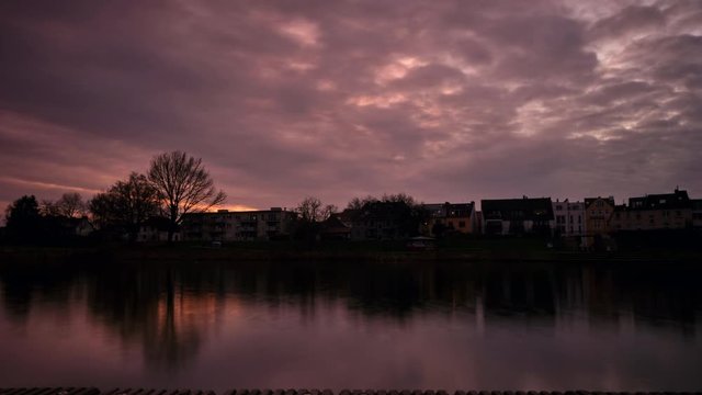 Colourful purple and orange lake time lapse with impressive cloud movement and vividly coloured houses in the background