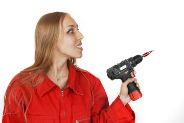 Beautiful blond young woman in red overalls, holding a drill tool in hands, isolated on white background