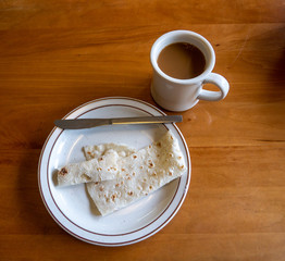 Top down view of a plate with traditional scandinavian potato lefse and a butter knife, and a cup of coffee on a wooden table.