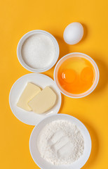 Ingredients for baking on an orange background, top view, minimal style. Flour, eggs, sugar and butter in white bowls. Cooking and baking concept, flat lay