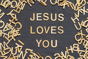 wooden letters JESUS LOVES YOU on slate background