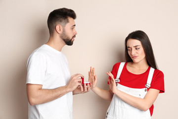 Young woman rejecting engagement ring from boyfriend on beige background