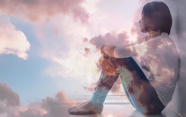 Obraz premium Memories of freedom. A melancholic adult woman is sitting on a windowsill and hugging her knees while looking through the window and thinking about the past. Double exposure.