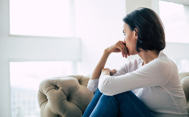 Trying to cope. Close-up photo of an adult woman who turned away from the camera, looking through the window with sadness.