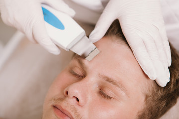 Naklejka premium Cropped close up of a dermatologist using ultrasound cleaning device on forehead of a male client