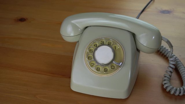 A retro rotary phone on a wood table. The camera start with a pan to the classic phone, then a hand pick up the call and later hanging classic telephone dial. Handset with long coiled cable.