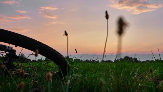 Colourful sunset time lapse with cloud frontal development and light shining through. A bike tyre and natural grasses are in the foreground 