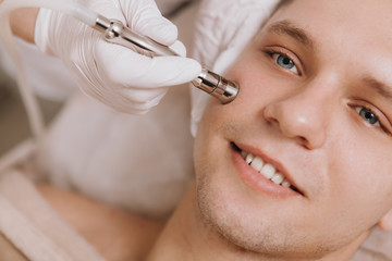 Naklejka premium Cropped close up of a young cheerful man smiling while cosmetologist performing facial skincare treatment