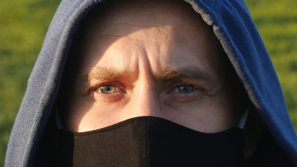 The Young Caucasian Man in Hoodie and Black Face Mask Outdoors Close up Portrait. Concept of Healthy, Safety Life, Virus protection, Spreading Pandemic and World Panic Safety