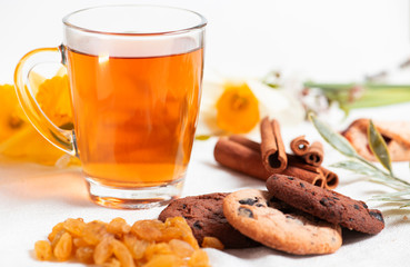 Morning breakfast. Cup of tea , raisin, cinnamon stick, cookies with chocolate on the white  background and spring flowers.
