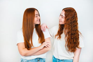 two redheaded young women standing on isolated white backgroung, one is holding her arm on friend's shoulder, both smiling, support concept