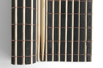 Chinese sticks lie on a black and white partially twisted bamboo wooden rug. Objects for sushi. View from above. Asian traditions. Background in blur.