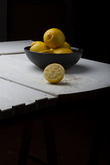 Yellow lemons in a black bowl, on a white wooden table.