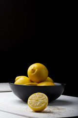 Yellow lemons in a black bowl, on a white wooden table.