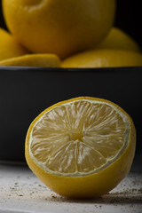 Yellow lemons in a black bowl, on a white wooden table.