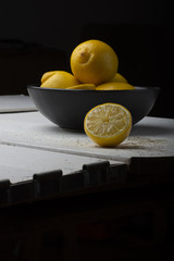 Yellow lemons in a black bowl, on a white wooden table.