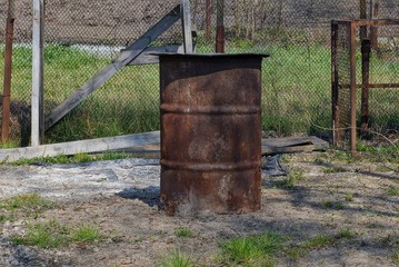 one big old iron barrel in brown rust stands on gray ground and grass outside