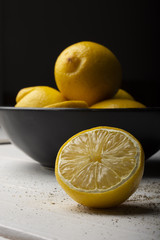 Yellow lemons in a black bowl, on a white wooden table.