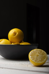 Yellow lemons in a black bowl, on a white wooden table.