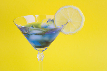 Iced blue drink  with lemon in a martini  glass on the yellow background. Closeup.