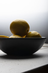 Yellow lemons in a black bowl, on a white wooden table.