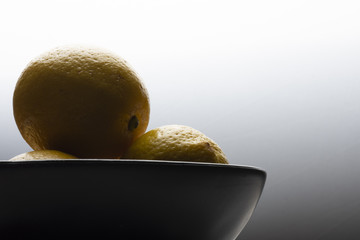 Yellow lemons in a black bowl, on a white wooden table.