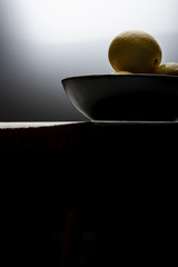 Yellow lemons in a black bowl, on a white wooden table.