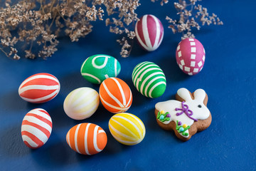 Attributes of the chrestian Easter holiday - colored eggs and gingerbread in the form of a rabbit on a dark blue background