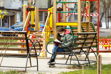 Fototapeta na wymiar A masked teenage girl is reading a book in the playground.