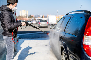 washing car by water pressure at self-service station. A man with a respirator on the face protects...