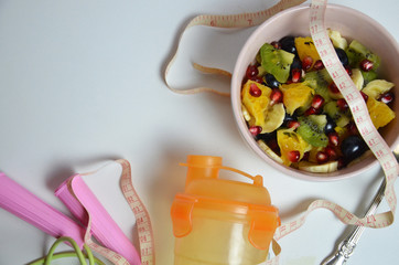 Fitness, healthy fruits, Fresh healthy salad, diet and active lifestyles Concept, dumbbells, fresh fruits, bottle for water, measure centimeter, jump rope on a white background . copy space for text.