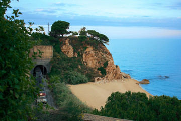 Sandy beach bay with rocks. Train leaving the tunnel. The combination of nature with technological progress.