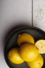Yellow lemons in a black bowl, on a white wooden table.