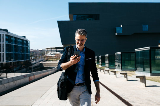 Gray-haired businessman walking with cell phone in the city