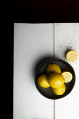 Yellow lemons in a black bowl, on a white wooden table.