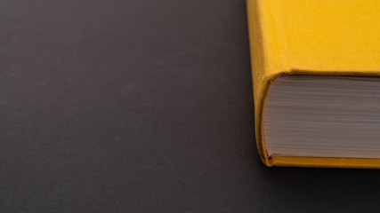 Yellow book on a matte black background. Binding of the book closeup. The book is on the right side of the frame. Copy space