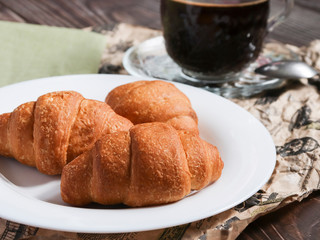 Croissants on a white plate and wooden table close-up. The concept of the perfect delicious breakfast or lunch.