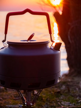 Boiling water in a touristic kettle outdoors next to the water at sunset.