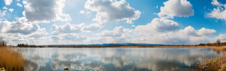 Panoramic landscape from the lake shore with colorful clouds in the spring sun.