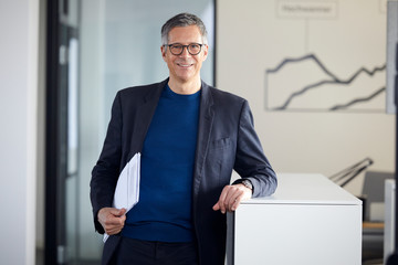 Portrait of smiling businessman holding papers in office