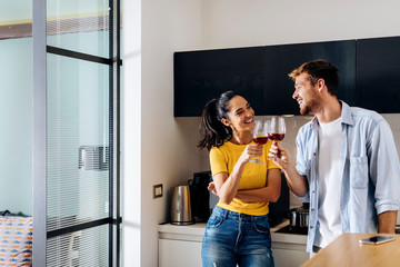 Happy young couple drinking wine in the kitchen at home together