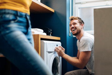 Happy young man looking at girlfriend and doing the laundry at home