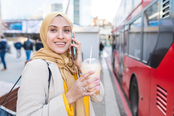 Portrait of smiling young woman on the phone waiting at bus stop