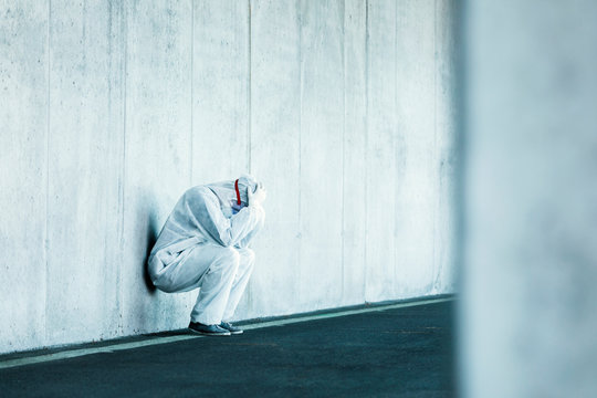 Despaired man wearing protective clothing leaning against concrete wall