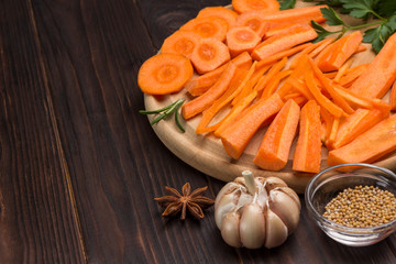 Obraz na płótnie Canvas Raw chopped carrots on cutting board. Garlic and mustard seeds on table.