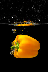 Big yellow bell pepper falls into the water.Fresh yellow paprika splash in water on black background