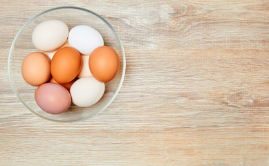 eggs of different colors from white to brown in a glass bowl on a wooden table surface